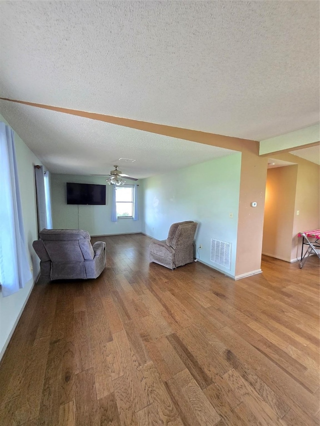 1495 W Bayshore Dr, Palacios, TX 77465 - unfurnished living room with wood finished floors, a textured ceiling, ceiling fan, and baseboards