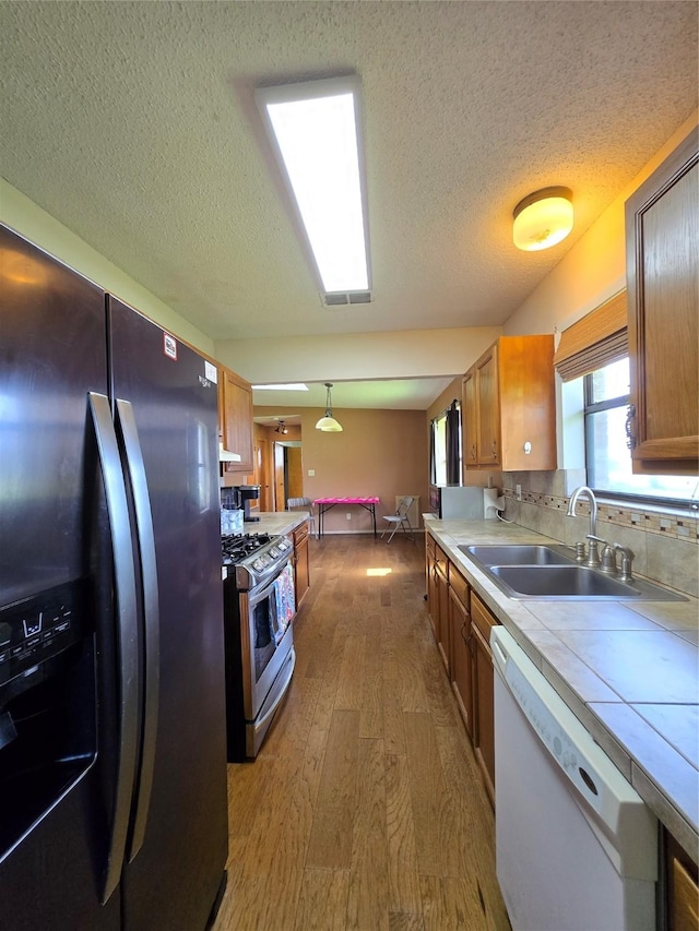 1495 W Bayshore Dr, Palacios, TX 77465 - kitchen with stainless steel appliances, a sink, tile counters, dark wood finished floors, and brown cabinets
