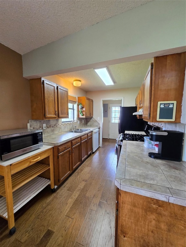 1495 W Bayshore Dr, Palacios, TX 77465 - kitchen featuring appliances with stainless steel finishes, wood finished floors, brown cabinetry, a sink, and light countertops