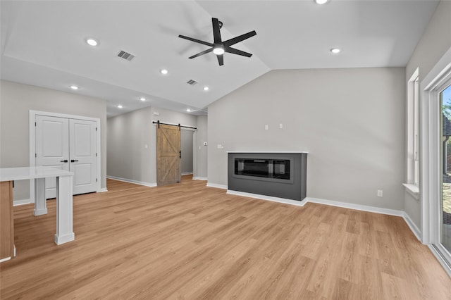 unfurnished living room with ceiling fan, a barn door, light wood-type flooring, and lofted ceiling