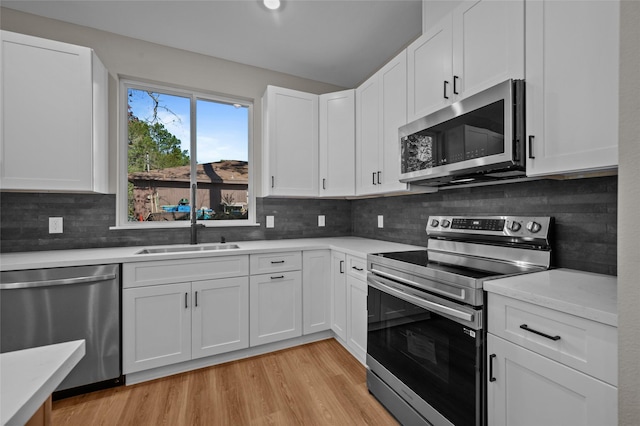 kitchen featuring appliances with stainless steel finishes, light hardwood / wood-style flooring, white cabinetry, and sink