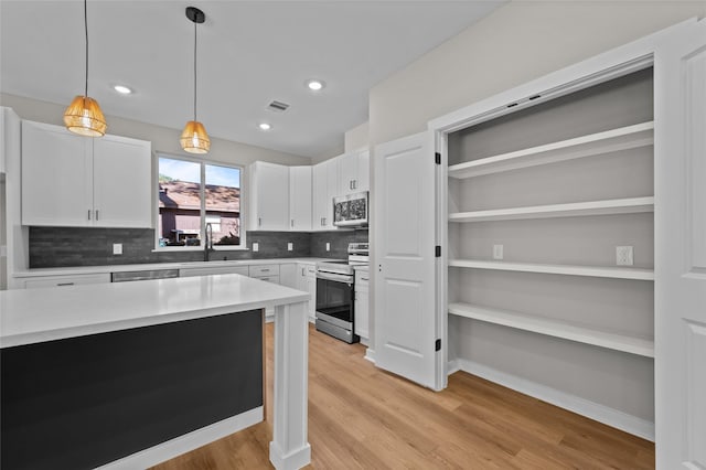 kitchen featuring appliances with stainless steel finishes, backsplash, light hardwood / wood-style floors, white cabinetry, and hanging light fixtures