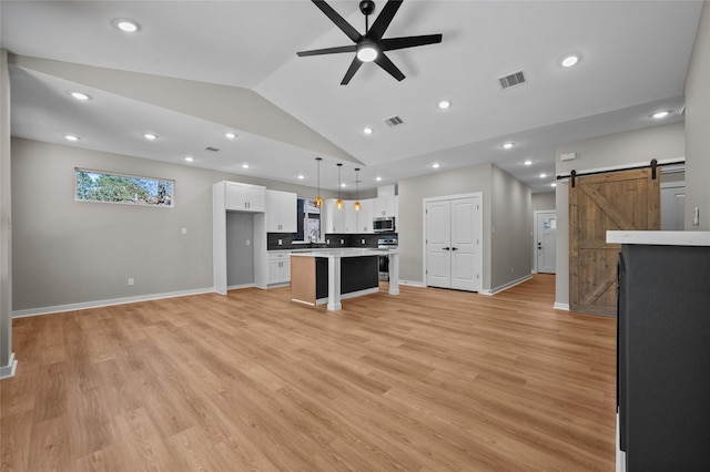 unfurnished living room with ceiling fan, sink, a barn door, vaulted ceiling, and light wood-type flooring