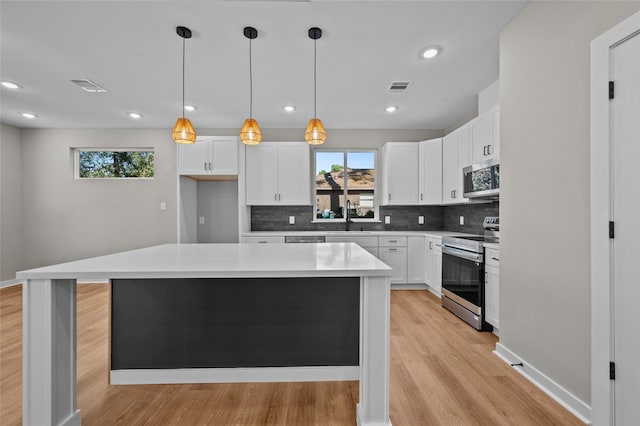 kitchen featuring white cabinetry, a center island, hanging light fixtures, light hardwood / wood-style floors, and appliances with stainless steel finishes