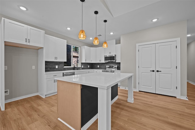 kitchen featuring pendant lighting, white cabinets, light hardwood / wood-style floors, appliances with stainless steel finishes, and a kitchen island