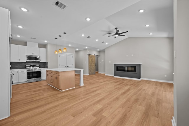 kitchen with white cabinetry, hanging light fixtures, stainless steel appliances, a barn door, and a kitchen island