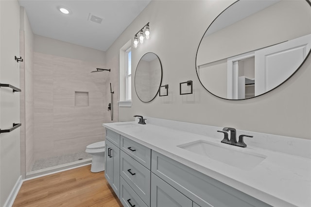 bathroom featuring a tile shower, vanity, hardwood / wood-style flooring, and toilet