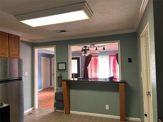 kitchen with stainless steel refrigerator, crown molding, and a textured ceiling