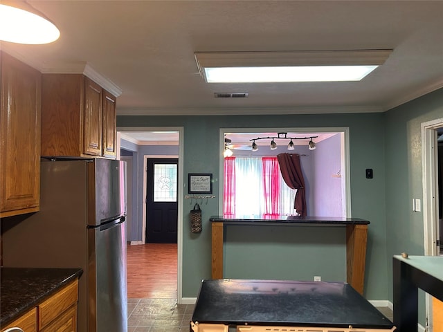 kitchen with light hardwood / wood-style floors, stainless steel refrigerator, crown molding, and dark stone countertops