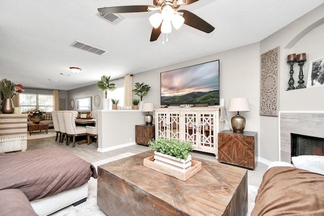 living room with a tiled fireplace, ceiling fan, and light hardwood / wood-style floors