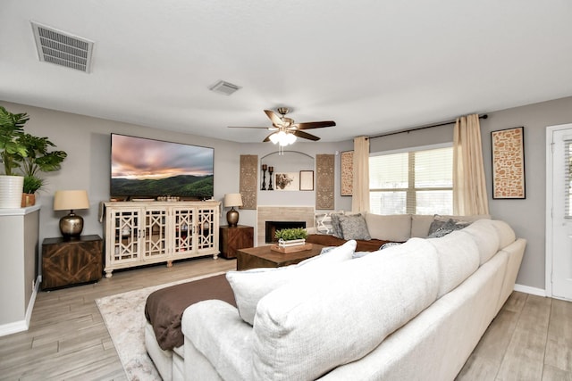 living room featuring ceiling fan, light wood-type flooring, and a tile fireplace