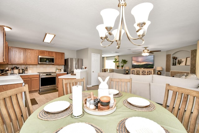 dining area with a textured ceiling, sink, ceiling fan with notable chandelier, and light wood-type flooring