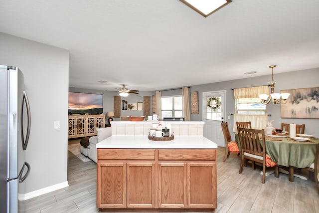 kitchen featuring stainless steel fridge, ceiling fan with notable chandelier, decorative light fixtures, light hardwood / wood-style flooring, and a center island