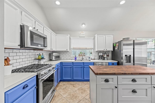 kitchen featuring appliances with stainless steel finishes, blue cabinets, sink, butcher block counters, and lofted ceiling