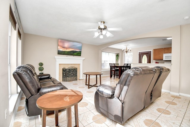 tiled living room featuring a fireplace and ceiling fan with notable chandelier