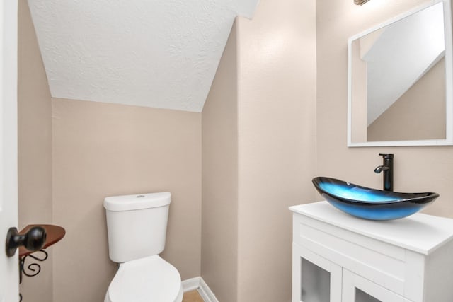 bathroom featuring vanity, a textured ceiling, toilet, and vaulted ceiling