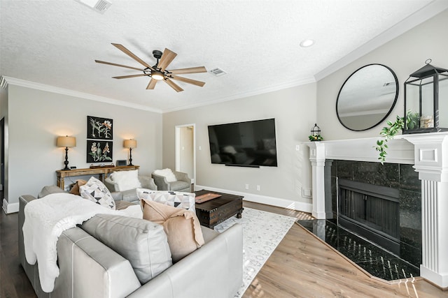 living room with ceiling fan, hardwood / wood-style floors, a textured ceiling, a tiled fireplace, and ornamental molding