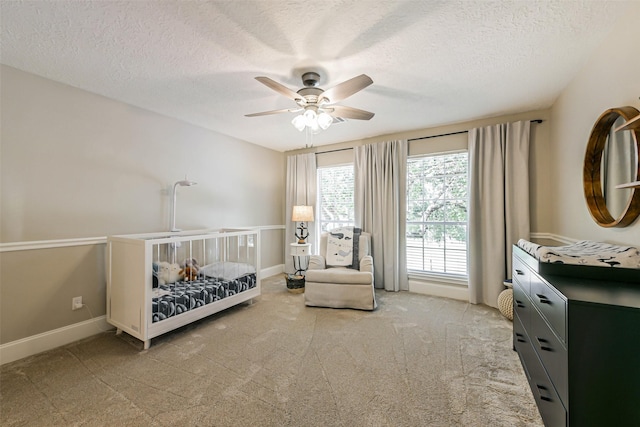 carpeted bedroom with ceiling fan, a nursery area, and a textured ceiling