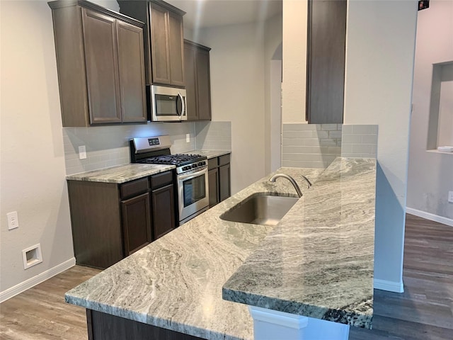 kitchen featuring appliances with stainless steel finishes, a sink, light stone counters, and tasteful backsplash