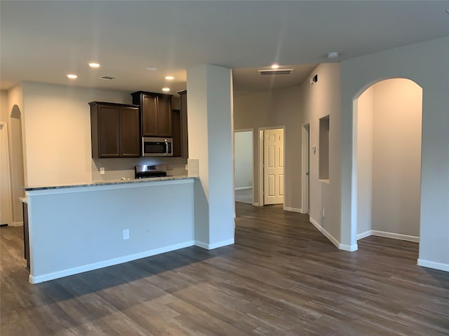 kitchen featuring dark brown cabinetry, appliances with stainless steel finishes, arched walkways, and dark wood finished floors