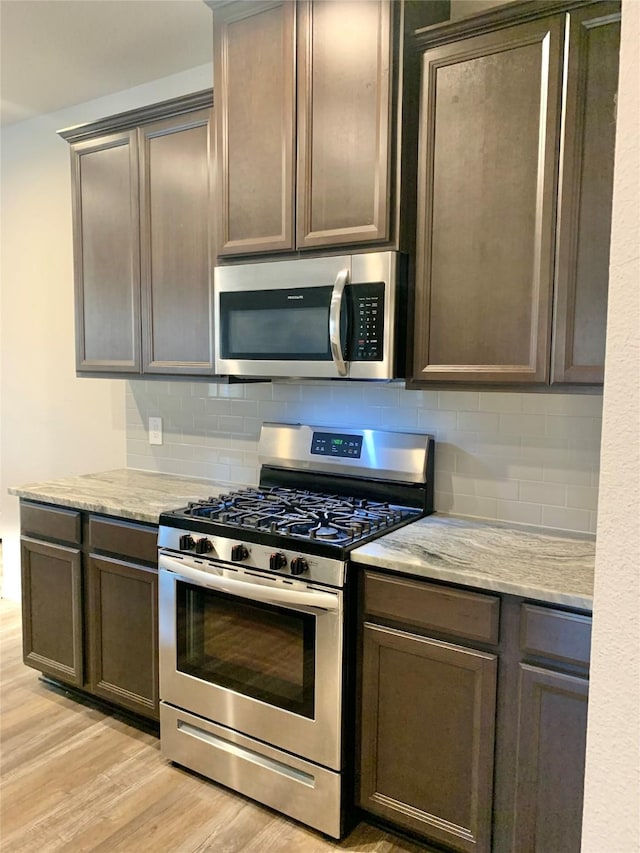 kitchen featuring stainless steel appliances, light wood-style flooring, decorative backsplash, dark brown cabinets, and light stone countertops