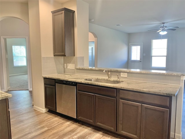 kitchen with light wood finished floors, backsplash, a sink, dishwasher, and a peninsula