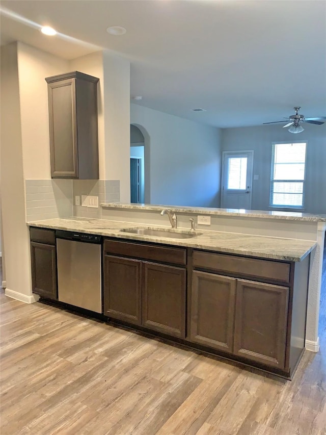 kitchen featuring arched walkways, a sink, light wood-style floors, light stone countertops, and dishwasher