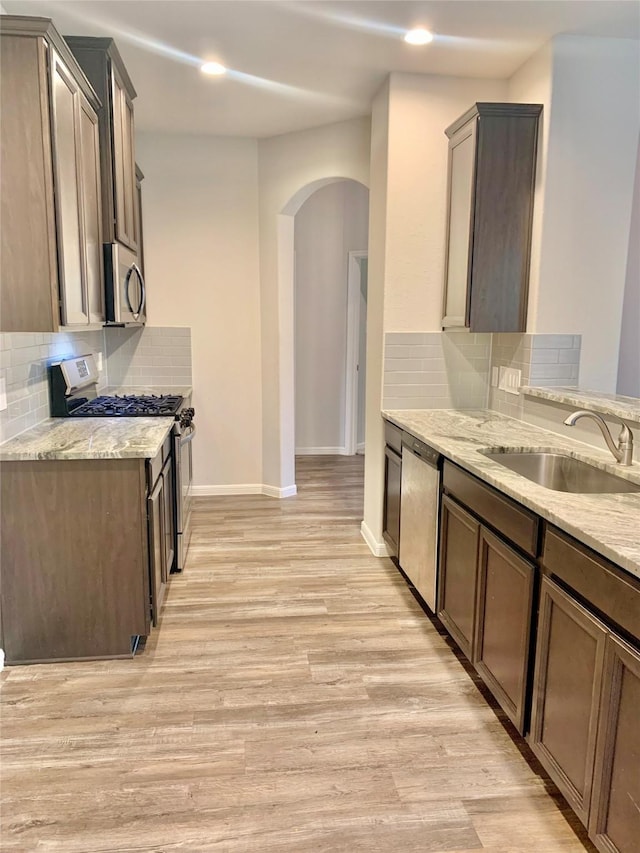 kitchen with stainless steel appliances, light wood-type flooring, a sink, and light stone countertops