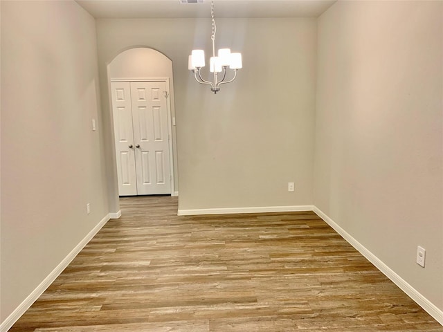 unfurnished room with arched walkways, a notable chandelier, visible vents, wood finished floors, and baseboards