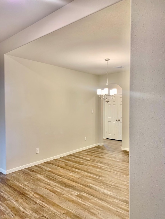 empty room with a chandelier, baseboards, visible vents, and light wood-style floors