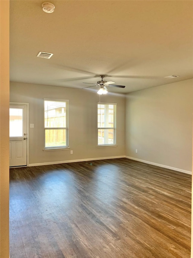 spare room with dark wood-type flooring, visible vents, plenty of natural light, and baseboards