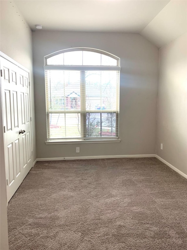 carpeted empty room featuring vaulted ceiling and baseboards