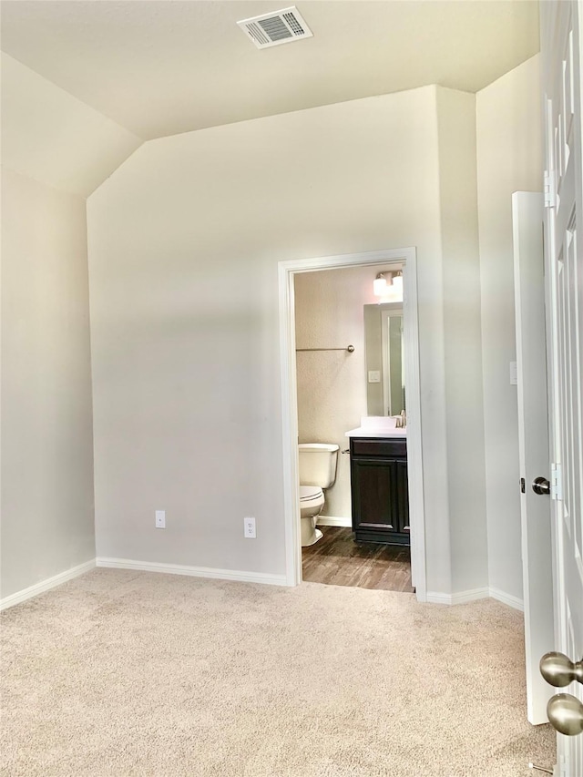 unfurnished bedroom with lofted ceiling, ensuite bathroom, visible vents, baseboards, and carpet