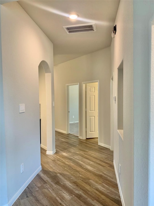 unfurnished room featuring baseboards, visible vents, arched walkways, and dark wood-style flooring