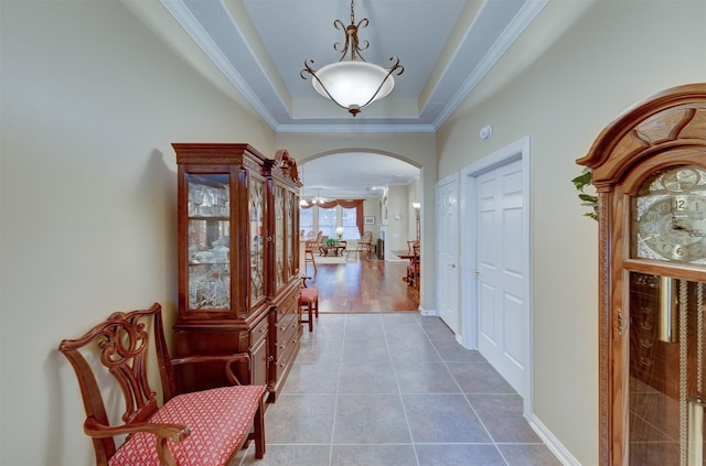 corridor with a tray ceiling, wood-type flooring, and ornamental molding