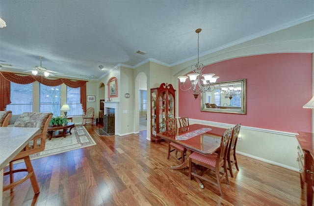 dining space with a fireplace, crown molding, hardwood / wood-style floors, and ceiling fan with notable chandelier