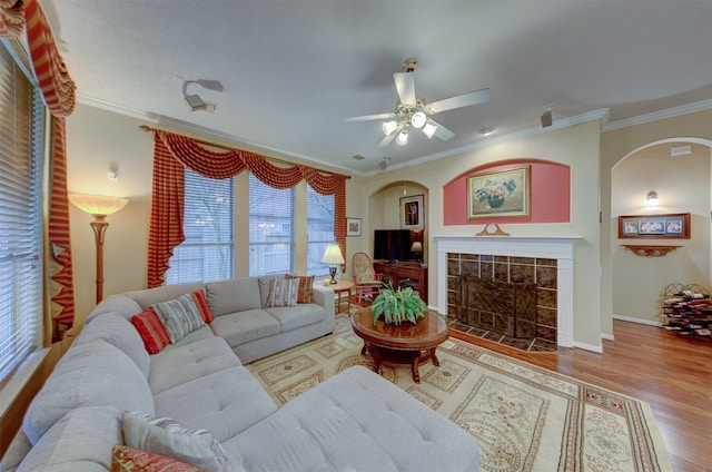 living room featuring a tiled fireplace, ceiling fan, ornamental molding, and hardwood / wood-style flooring