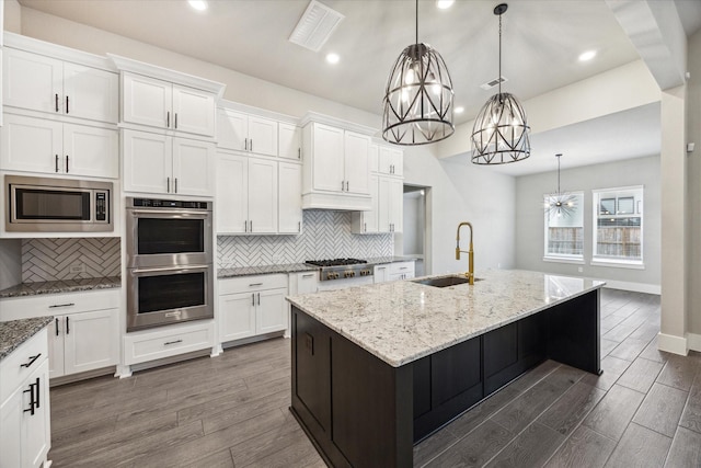 kitchen featuring stainless steel appliances, a kitchen island with sink, sink, decorative light fixtures, and white cabinets