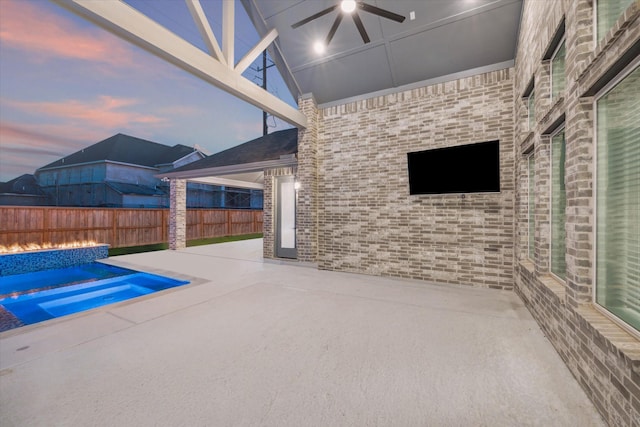 pool at dusk featuring ceiling fan and a patio