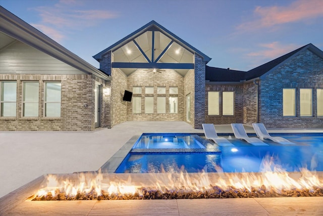 pool at dusk featuring ceiling fan, a patio, and a fire pit