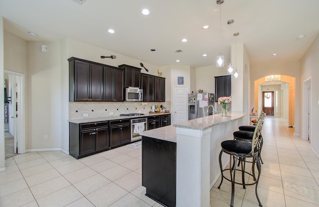 kitchen with light stone countertops, stainless steel appliances, tasteful backsplash, decorative light fixtures, and light tile patterned floors