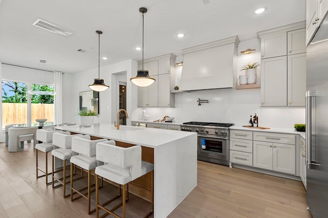 kitchen with sink, premium range hood, a center island with sink, and a kitchen breakfast bar