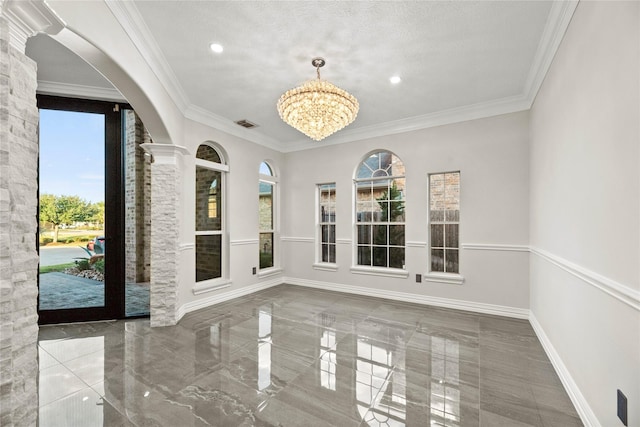 interior space featuring a notable chandelier, ornamental molding, a textured ceiling, and decorative columns