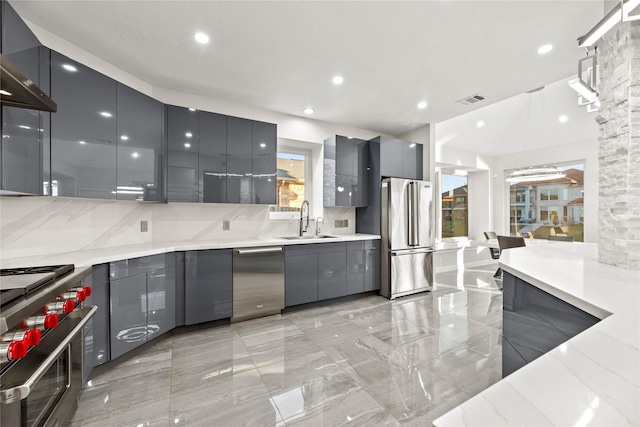 kitchen featuring light stone countertops, appliances with stainless steel finishes, backsplash, sink, and gray cabinets