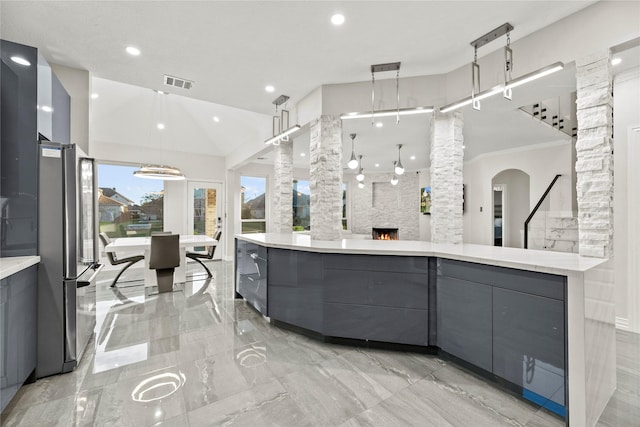 kitchen featuring gray cabinetry, stainless steel fridge, crown molding, decorative light fixtures, and a fireplace