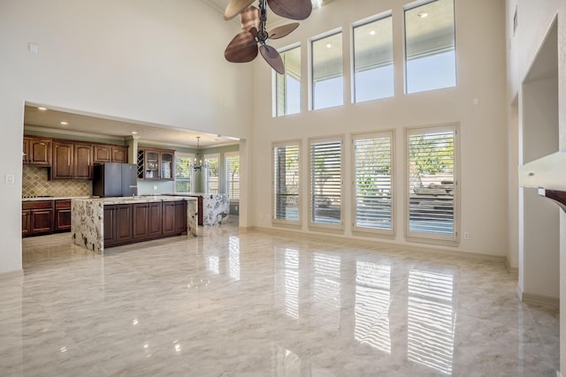 unfurnished living room featuring ceiling fan with notable chandelier, marble finish floor, a high ceiling, and baseboards