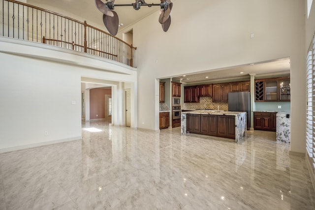 unfurnished living room with marble finish floor, a high ceiling, and baseboards