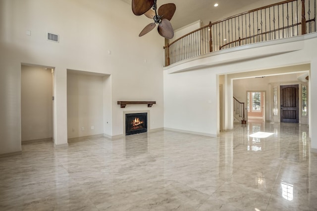 unfurnished living room featuring baseboards, visible vents, a glass covered fireplace, a towering ceiling, and marble finish floor