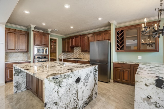 kitchen with light stone counters, glass insert cabinets, stainless steel appliances, a center island with sink, and crown molding