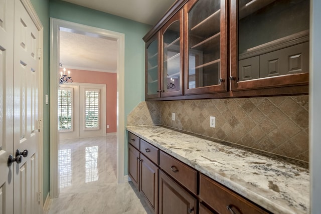 kitchen with tasteful backsplash, glass insert cabinets, light stone countertops, marble finish floor, and crown molding